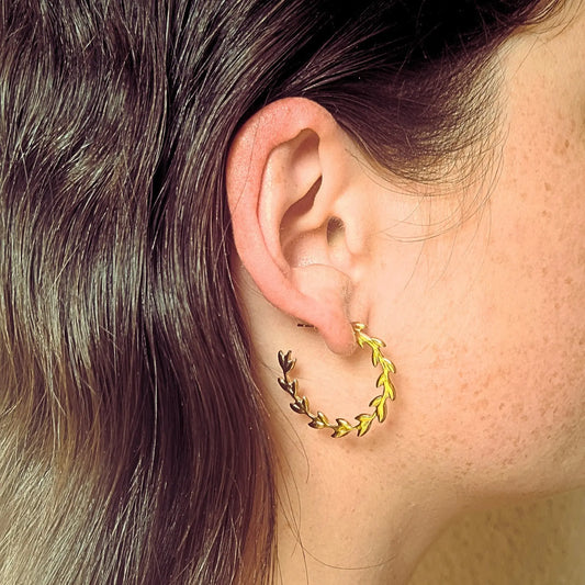 Paire de boucles d’oreilles créoles en acier inoxydable doré, ornées de motifs de feuilles façon couronne de laurier.