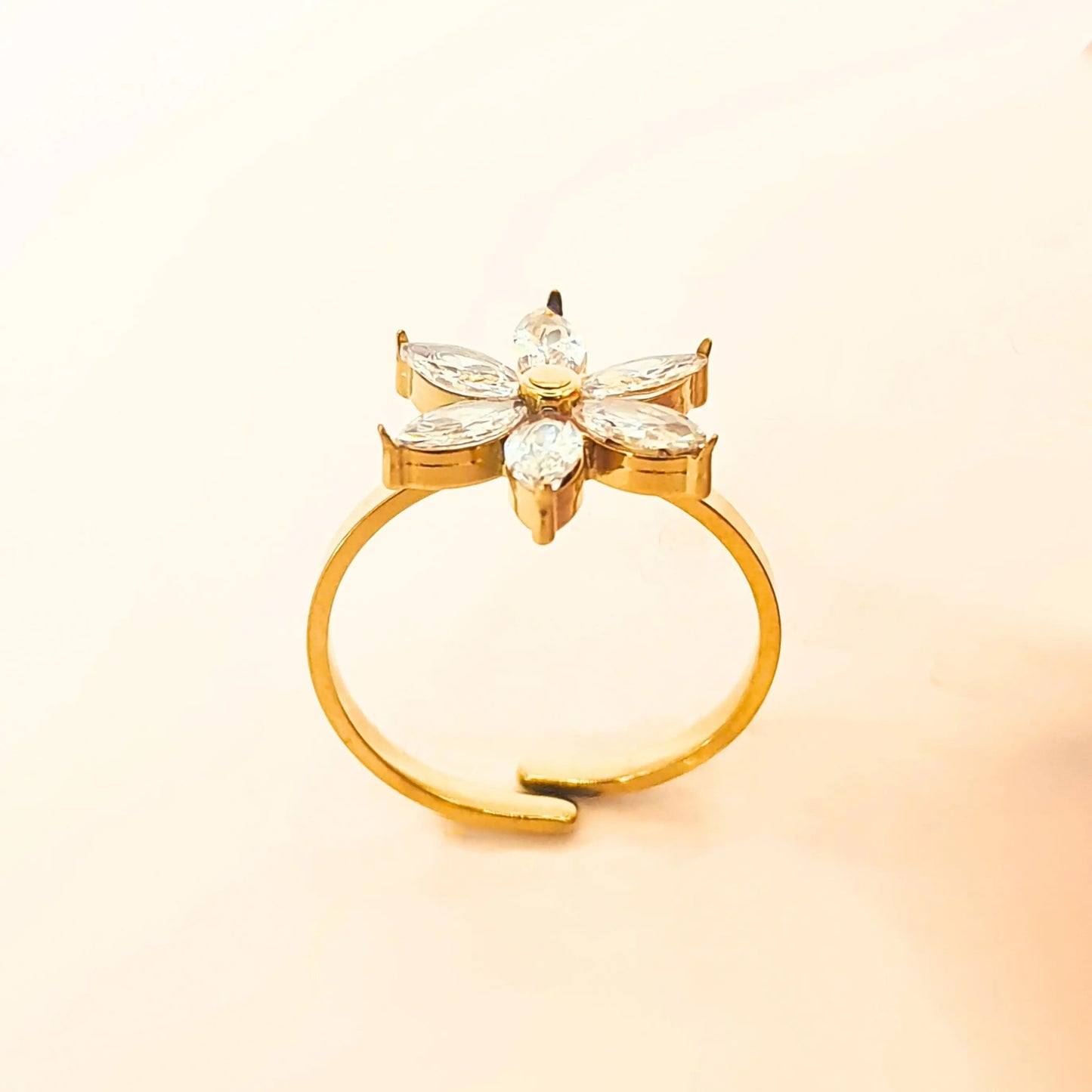 Bague fleur ajustable à toutes tailles de doigt en acier doré, pétales sertis de pierres zircons, résistante à l’eau et hypoallergénique, design élégant Eclosia Bijoux, fond beige