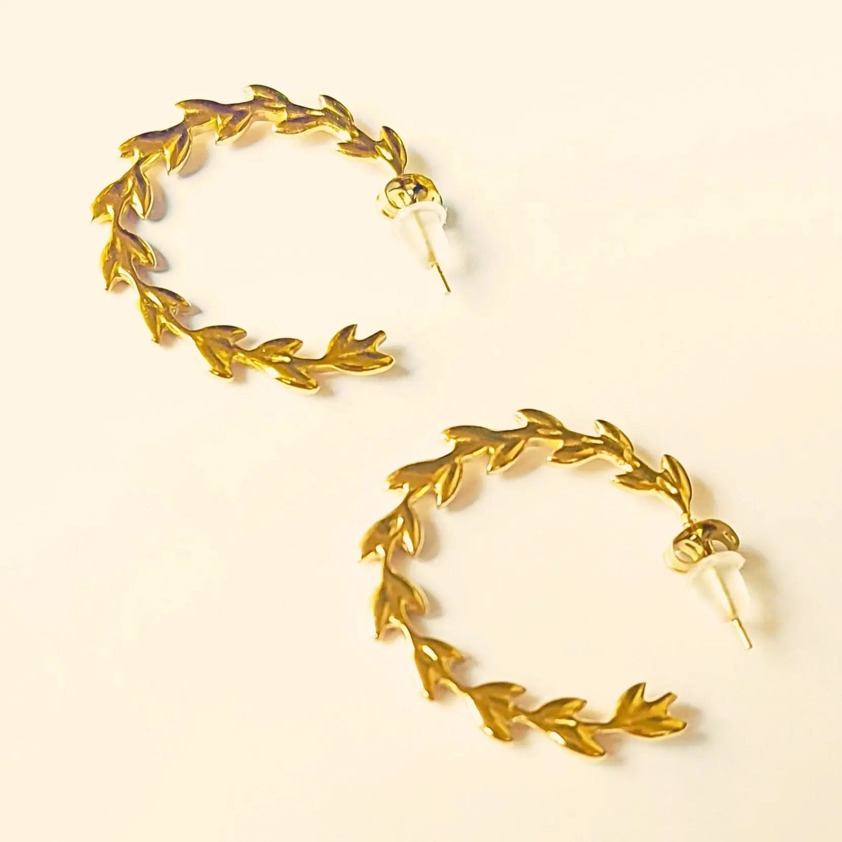 Paire de boucles d’oreilles créoles en acier inoxydable doré, ornées de motifs de feuilles façon couronne de laurier.