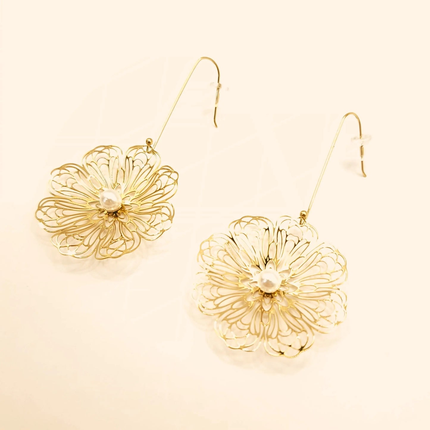 Paire de boucles d’oreilles pendantes en acier inoxydable doré, en forme de grandes fleurs ajourées avec perle blanche au centre.