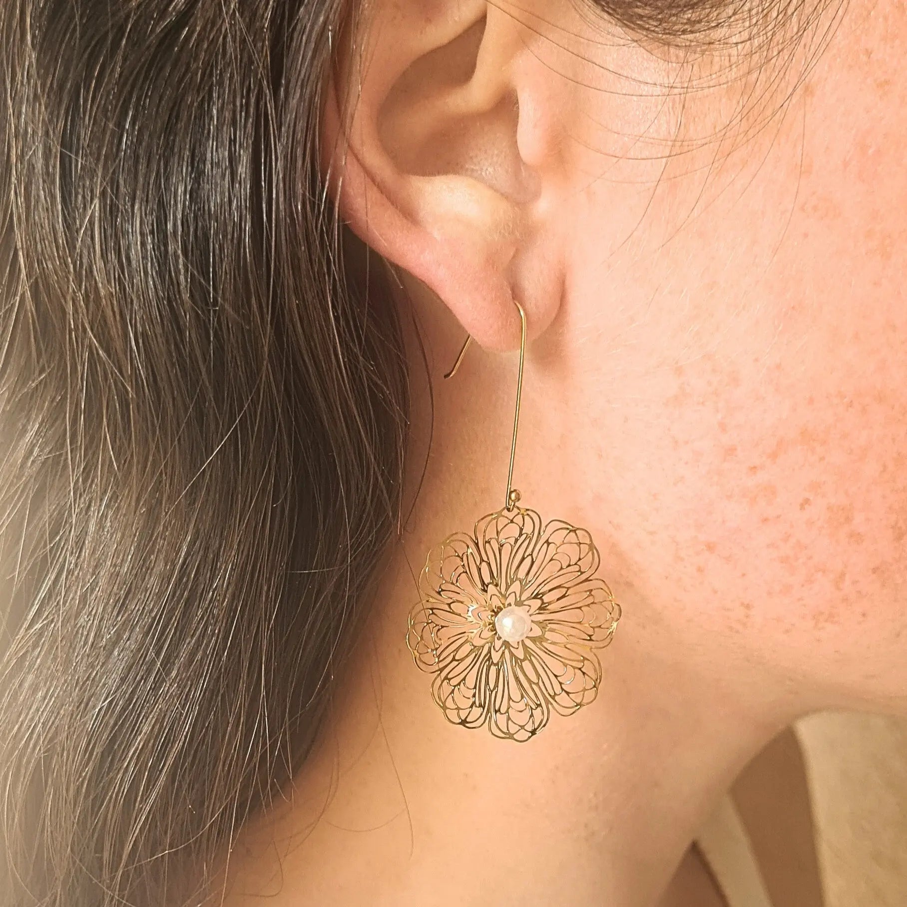 Paire de boucles d’oreilles pendantes en acier inoxydable doré, en forme de grandes fleurs ajourées avec perle blanche au centre.
